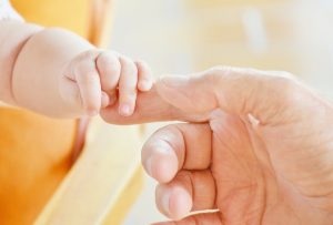 close up of baby and parent touching hands 