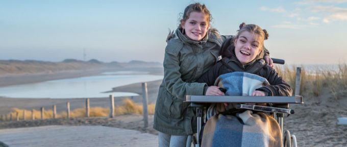 young girl in wheelchair on the beach with her friend