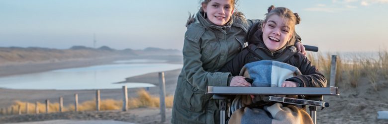 young girl in wheelchair on the beach with her friend