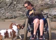 woman in wheelchair with 2 dogs on the beach