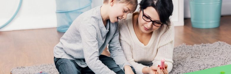 mother and autistic son playing with colouring chalks at home