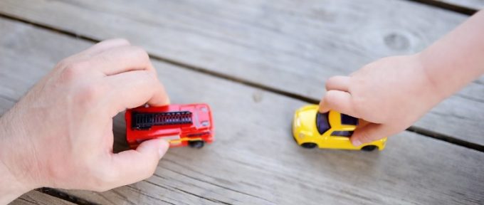 father's hand and child's hand playing with toy cars