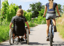 man in wheelchair with woman on bike doing some exercise