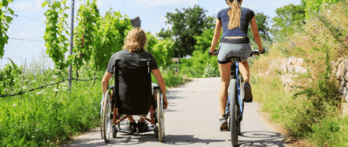 man in wheelchair with woman on bike doing some exercise