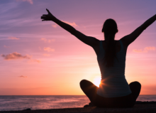 Person combatting stress by meditating by the sea and sunset