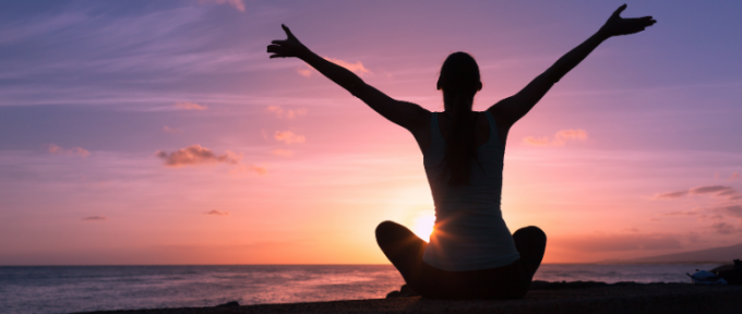 Person combatting stress by meditating by the sea and sunset