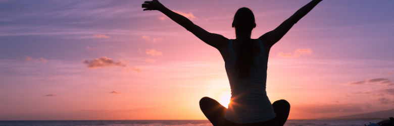 Person combatting stress by meditating by the sea and sunset