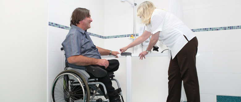 Person in wheelchair being shown how to use an accessible bathroom