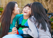 Boy in wheelchair laughing with his two sisters