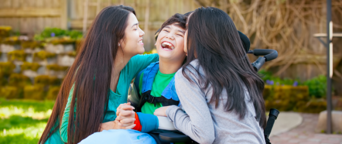 Boy in wheelchair laughing with his two sisters
