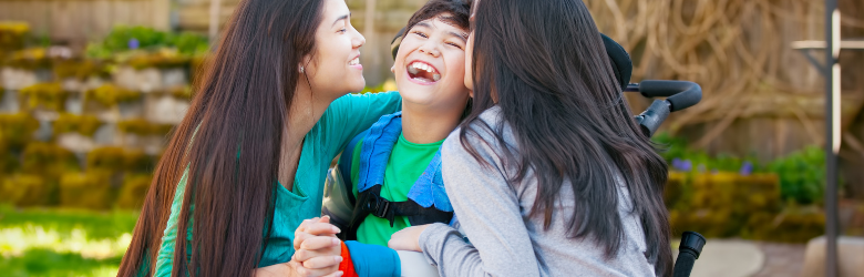 Boy in wheelchair laughing with his two sisters